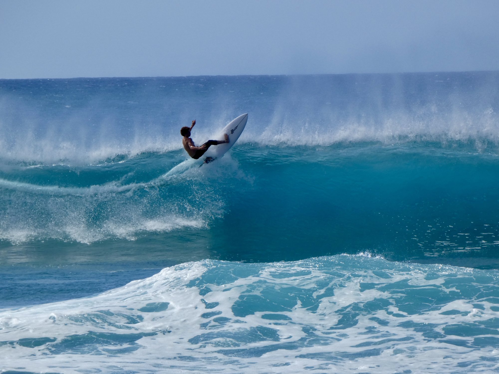 Surfer hitting the lip of a big turquoise wave, spray trailing off the crest