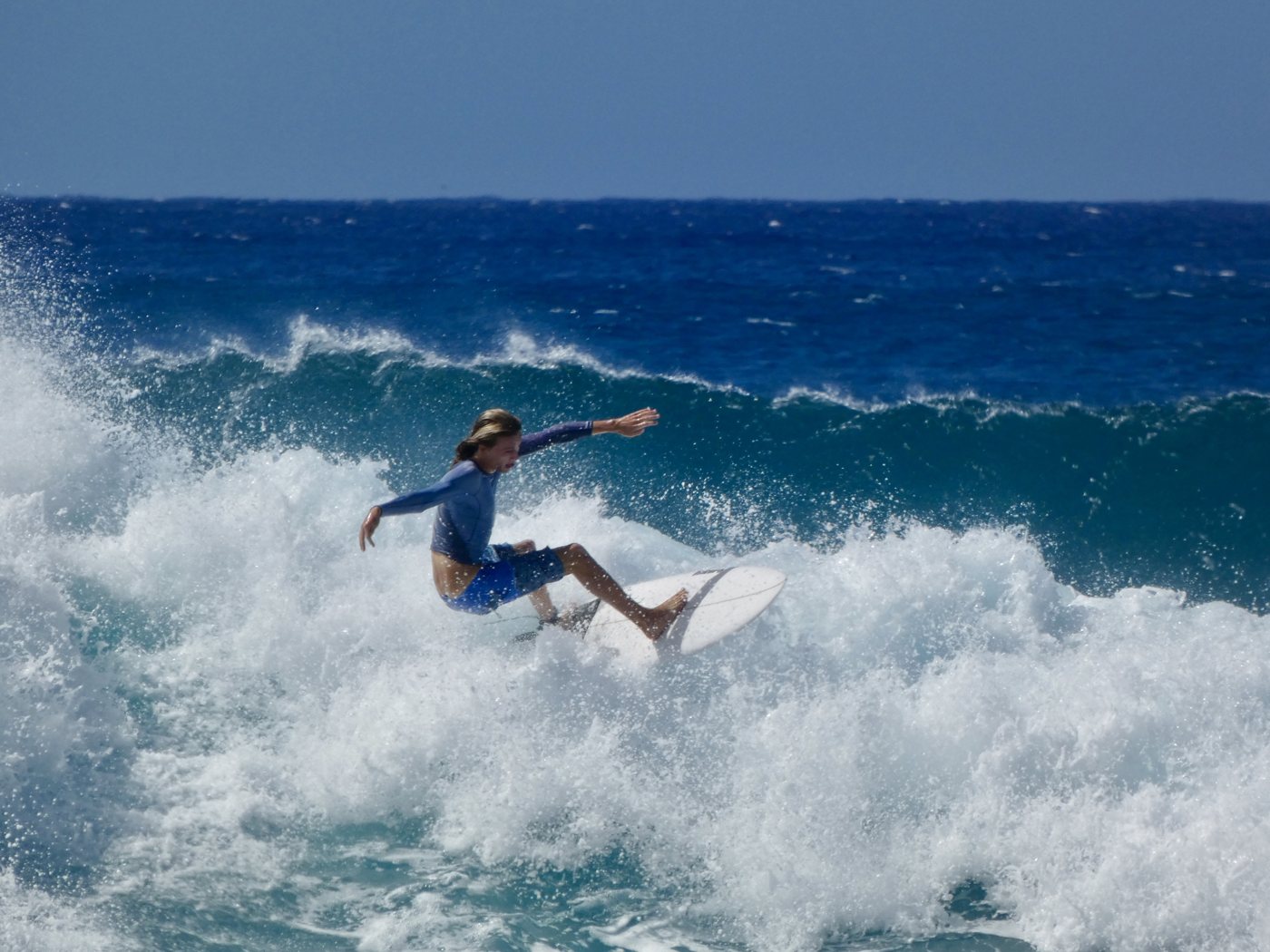 Surfer in a blue rash guard carving through whitewater