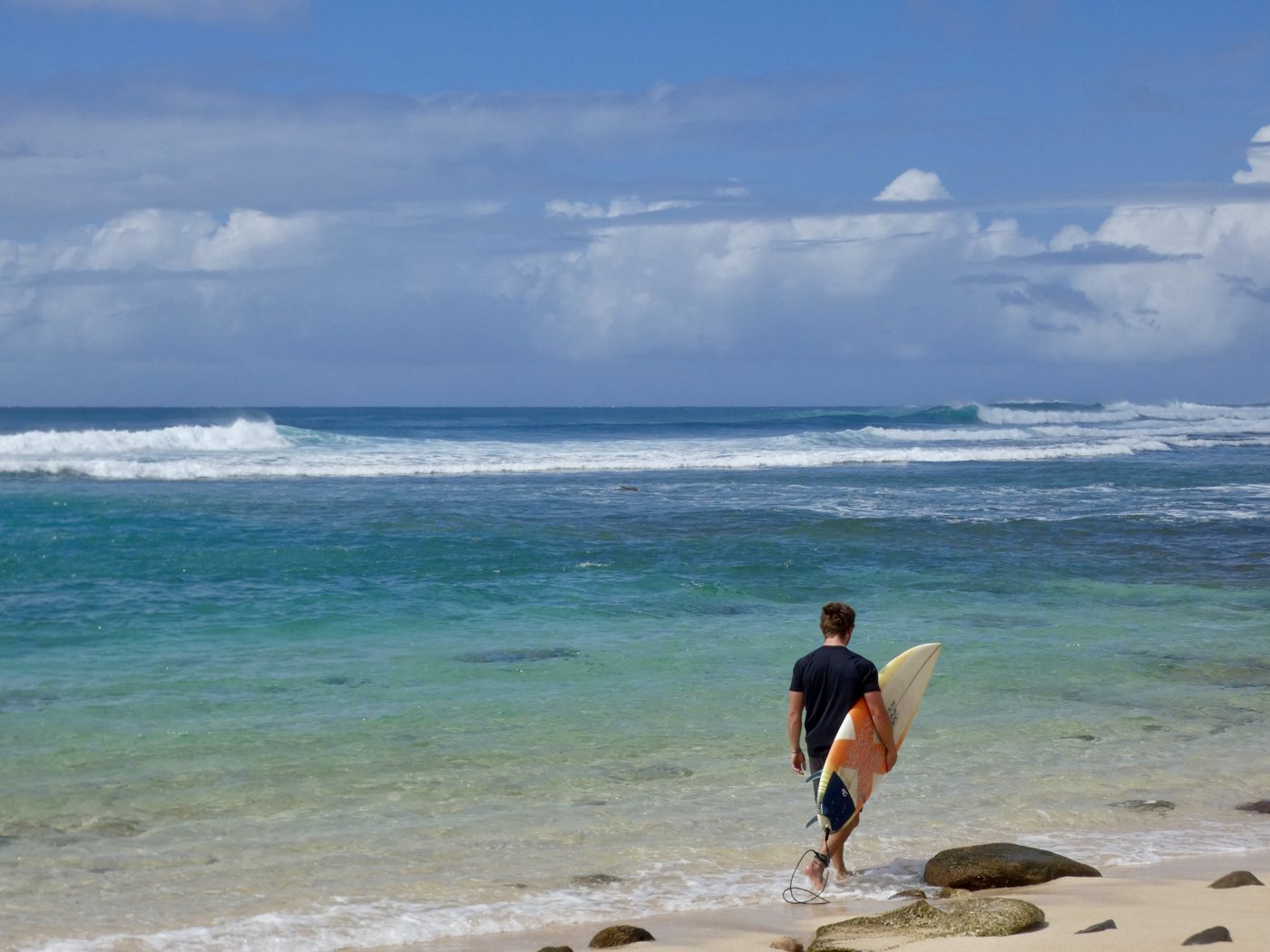 Surfer walking into turquoise water with a board under his arm