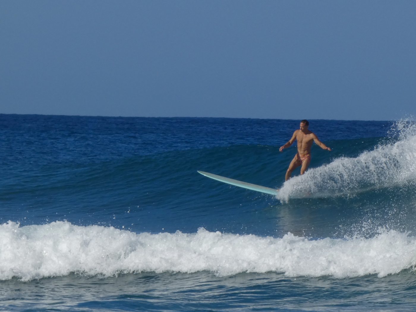 Longboarder trimming a clean blue wave