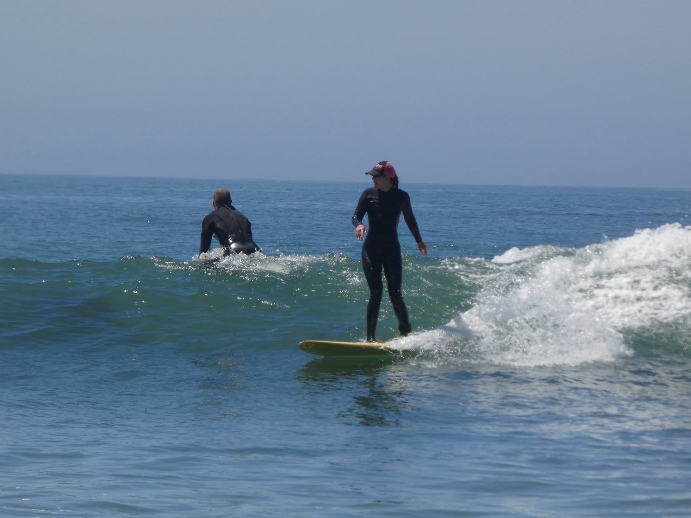 Surfer on a yellow longboard as another paddles past