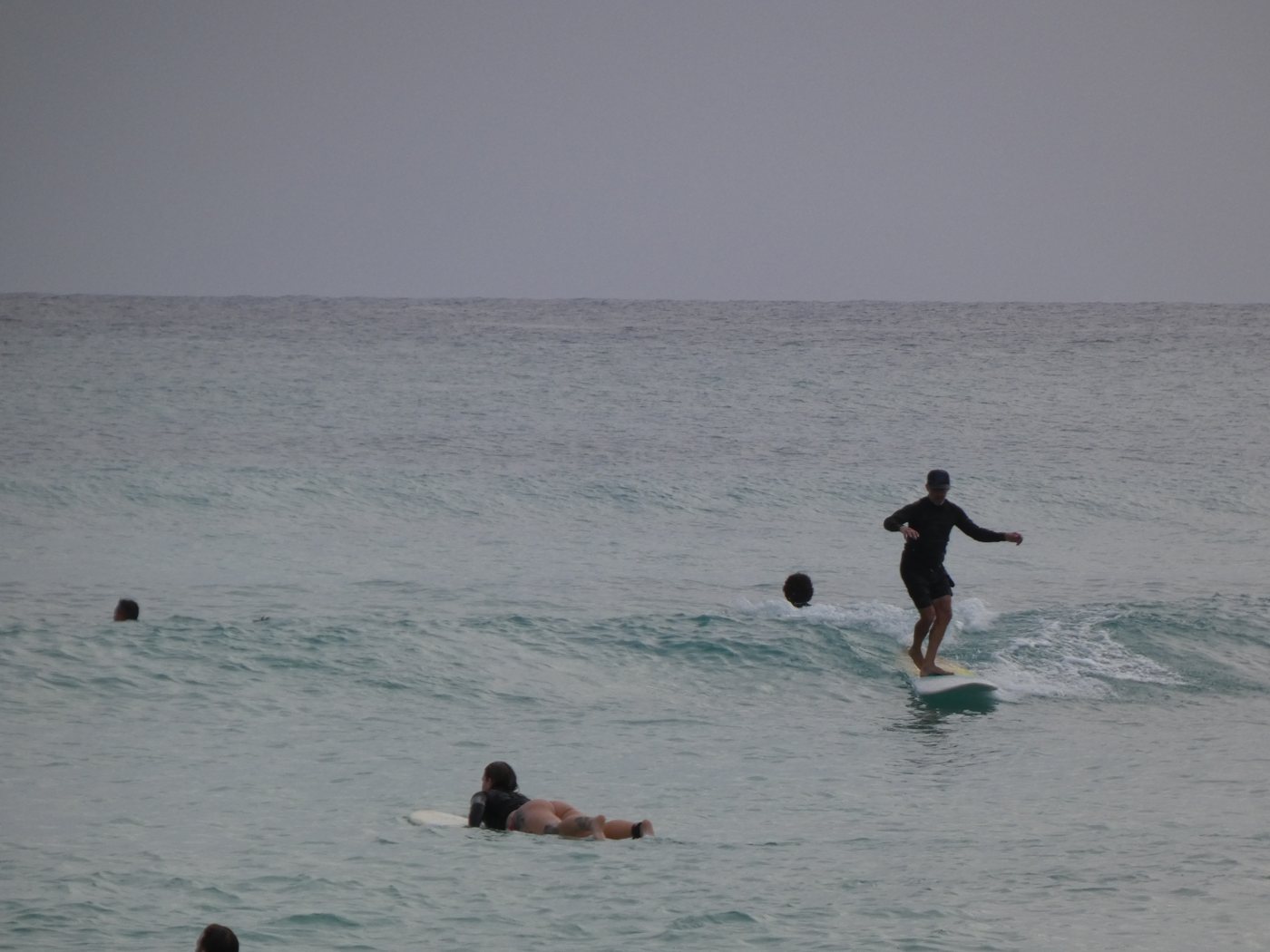 Longboarder in a cap cruising a soft wave as others paddle nearby