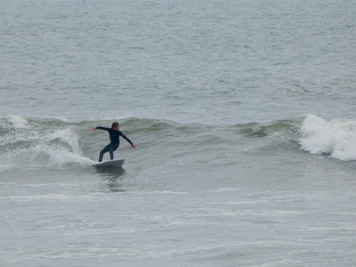 Young surfer in a wetsuit carving on a small grey wave