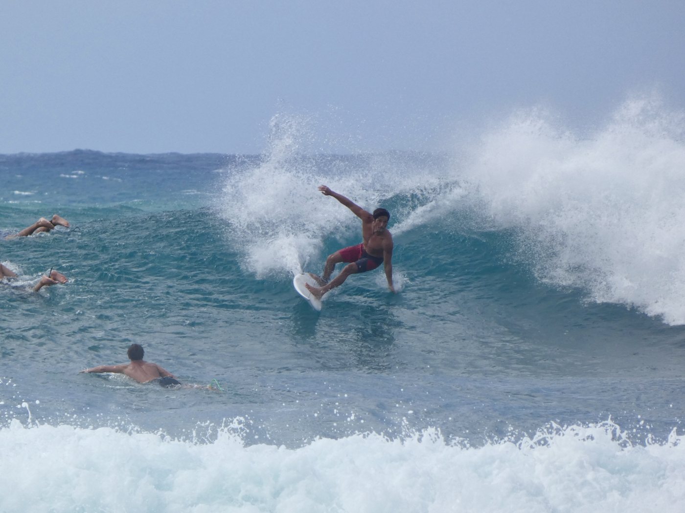 Surfer in red shorts throwing spray on a turn while others paddle out